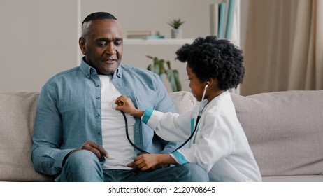 Little african american girl in medical gown plays sitting on couch kid doctor listens to father stethoscope pretends nurse having fun loving daughter forbids dad to smoke indicates get rid bad habit