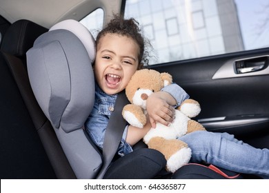 little african american girl with teddy bear sitting in car