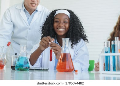 Little African Black Kids Learning Chemistry In School Laboratory. Teacher Man Teaching Clever Little Girl Doing A Chemical Science Experiment In A Laboratory On White Background