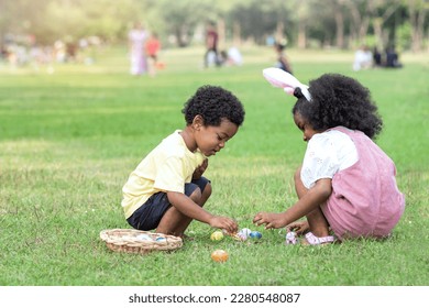 Little African boy and girl wearing bunny ears pick up Easter egg in garden, Easter eggs hunting outdoors - Powered by Shutterstock