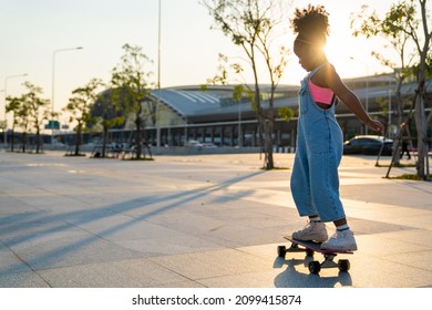 Little African child girl kid skating on skateboard at the park in the city. Happy cute preschool girl enjoy and having fun outdoor lifestyle practicing extreme sport skateboarding on summer vacation - Powered by Shutterstock