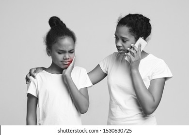 Little African Girl Suffering From Tooth Pain, Her Teen Sister Calling Dentist, Black And White Photo With Red Sign, Grey Studio Background