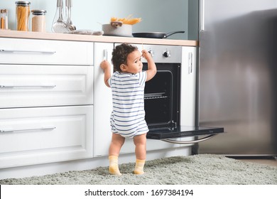 Little African-American baby near stove in kitchen. Child in danger