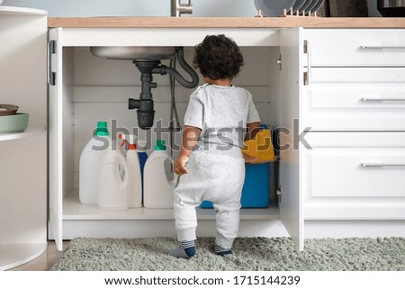 Little African-American baby playing with detergents at home. Child in danger