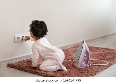 Little African-American Baby Playing With Socket And Iron At Home. Child In Danger