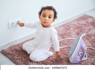 Little African-American Baby Playing With Socket And Iron At Home. Child In Danger