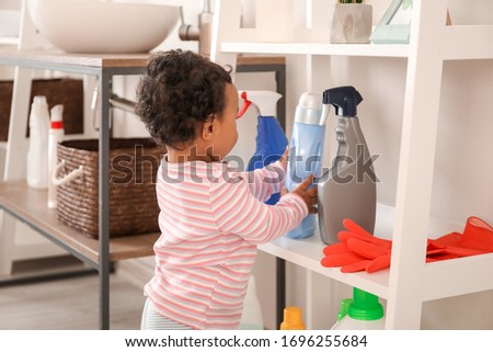 Little African-American baby playing with washing liquids at home. Child in danger