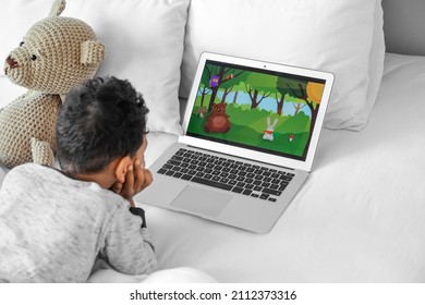 Little African-American boy with laptop watching cartoons on bed