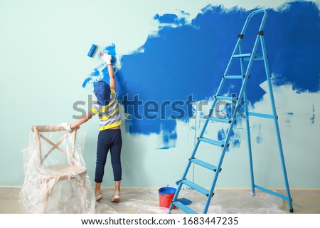 Little African-American boy painting wall in room