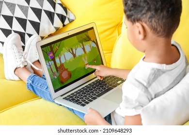 Little African-American boy pointing at laptop while watching cartoons on sofa at home - Shutterstock ID 2109648293