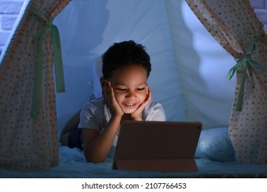 Little African-American boy watching cartoons on tablet computer in play tent at night - Powered by Shutterstock