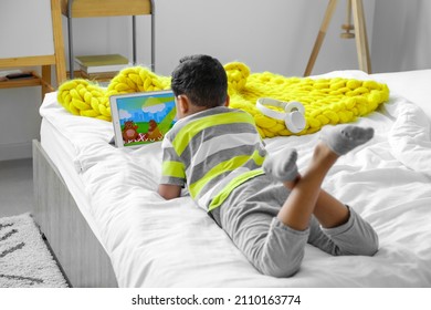 Little African-American boy watching cartoons on tablet computer in bedroom - Shutterstock ID 2110163774