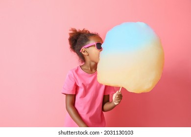 Little African-American girl eating cotton candy on color background - Shutterstock ID 2031130103