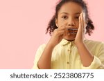 Little African-American girl playing harmonica on pink background, closeup