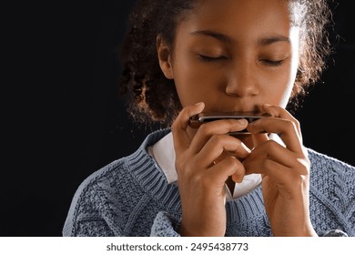 Little African-American girl playing harmonica on dark background, closeup - Powered by Shutterstock