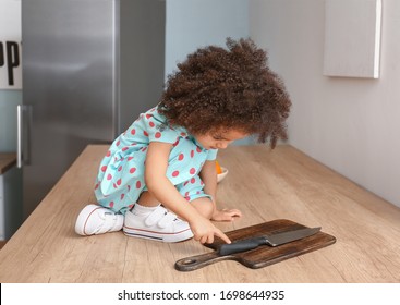 Little African-American Girl Playing With Knife In Kitchen. Child In Danger