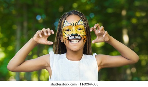 Little african-american girl with tiger face painting roaring, making funny grimace outdoors, copy space - Powered by Shutterstock