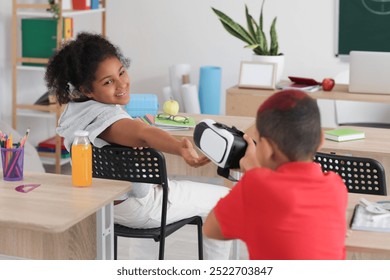 Little African-American schoolgirl taking VR glasses from her classmate in classroom - Powered by Shutterstock