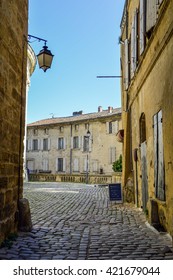 Little Alley With Cobblestones, A Lantern And Old Stone Buildings In Uzès, France.