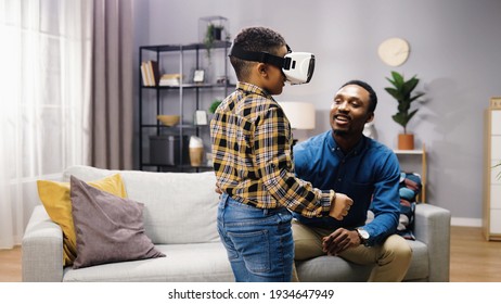 Little amazed African American boy teen wearing VR glasses standing in living room at home with young happy father, child in virtual reality headset using 3D futuristic technology, tech concept - Powered by Shutterstock