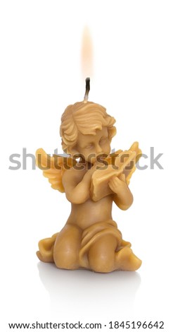 A little angel made of beeswax. With a burning wick on his head. A candle, angel reading a book. Isolated on white background with shadow reflection. With clipping (vector) path. All Saints' Day theme