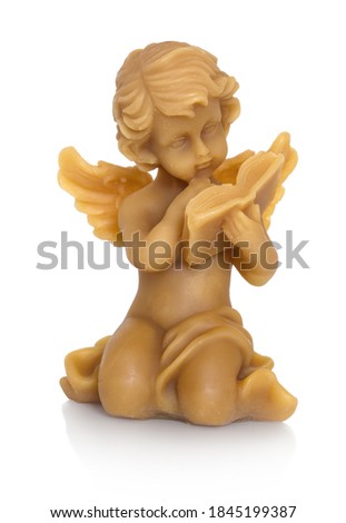 A little angel made of beeswax. Angel reading a book. Isolated on white background with shadow reflection. With clipping (vector) path. All Saints' Day theme