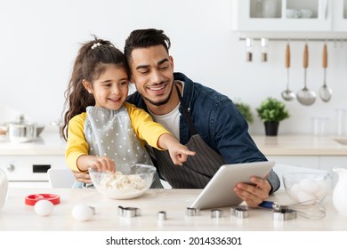 Little Arab Girl And Her Dad Checking Dough Online Recipe On Digital Tablet While Baking Pastry In Kitchen Together, Middle Eastern Father And Daughter Enjoying Cooking At Home, Free Space