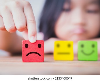 Little Asia Child Girl Choose Unhappy, Sad, Upset Face, Blurred Neutral And Happy Face Icon On Wood Cube. Concept Of Unhappy, Sad, Upset, Children, Kid, Family, Childrens Day.