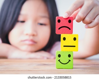 Little Asia Child Girl Putting Unhappy, Sad, Upset Face On Top Of Neutral And Happy Face Icon On Wood Cube. Concept Of Unhappy, Sad, Upset, Children, Kid, Family, Childrens Day.