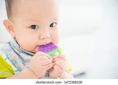 Little Asian Baby Biting Plastic Teether And Looking At Camera 