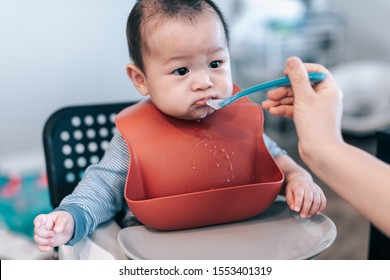 Little Asian Baby Boy With Red Bib Waiting For Food In Baby Chair