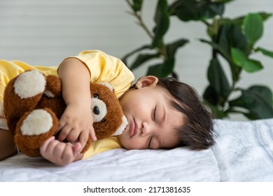 Little Asian Baby Girl Lying Down Sleeping On Bed At Home, Hugging Teddy Bear Doll. Newborn Child Relaxing In Bed. Nursery For Young Children.