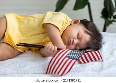 Little Asian Baby Girl Lying Down Sleeping On Bed At Home, With American Flag. Newborn Child Relaxing In Bed. Nursery For Young Children.