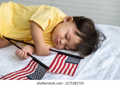 Little Asian Baby Girl Lying Down Sleeping On Bed At Home, With American Flag. Newborn Child Relaxing In Bed. Nursery For Young Children.