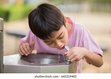 Little Asian Boy Drinking Water In The Public Park 