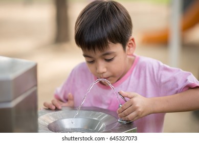 Little Asian Boy Drinking Water In The Public Park 