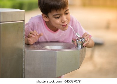 Little Asian Boy Drinking Water In The Public Park 