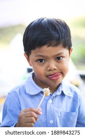 A Little Asian Boy Eating Sausage With A Bamboo Stick. 