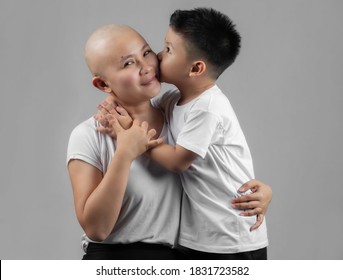 Little Asian Boy Kissing Mother, Young Cancer Patient, On The Cheek. Cancer And Family Support Concept.