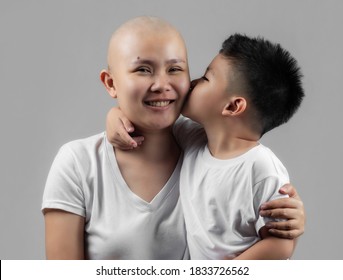 little Asian boy kissing mother, young cancer patient, on the cheek. Cancer and family support concept. - Shutterstock ID 1833726562