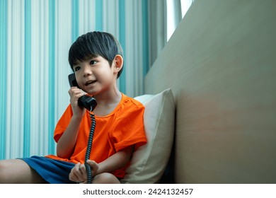 A little Asian boy lies on the bed talking on the phone. - Powered by Shutterstock