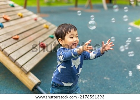 Little Asian boy is playing on the playground with happy face in summer and happily running around with soap bubbles
