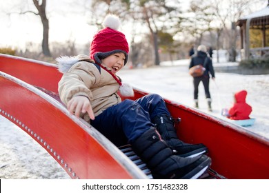 Little Asian Boy Playing Slide In Winter Time At Playground. Happy Kid Enjoying At Outdoor Park With Winter Clothes And Hat.