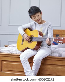 Little Asian Boy Sitting & Playing Guitar At Home