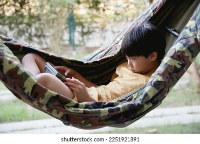 Little asian boy using a tablet computer while relaxing in a hammock - Shutterstock ID 2251921891