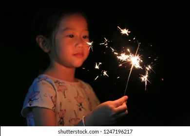 Little Asian child girl enjoy playing firecrackers. Focus at fire sparklers. - Powered by Shutterstock