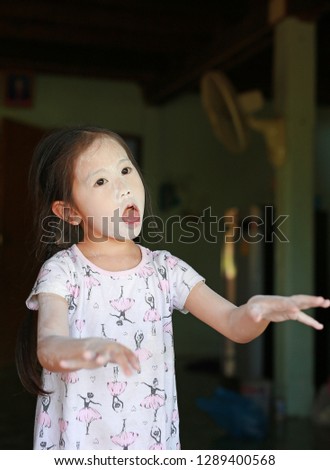 Little Asian child girl playing peekaboo with apply all her face with talcum powder.