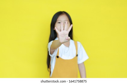 Little Asian Child Girl Showing Finger Number Four Isolated On Yellow Background. Kid Counting With Fingers For Education Concept. Selected Focus At His Hand