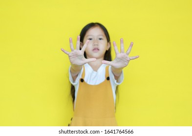 Little Asian Child Girl Showing Finger Number Ten Isolated On Yellow Background. Kid Counting With Fingers For Education Concept. Selected Focus At His Hand