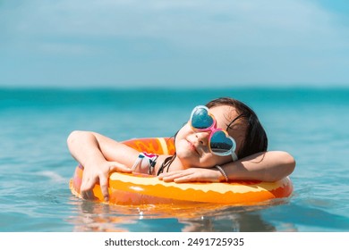 Little Asian child girl in swimwear and sunglasses with swim ring playing in the sea in summer sunny day. Happy children kid enjoy and fun outdoor lifestyle travel ocean on beach holiday vacation. - Powered by Shutterstock